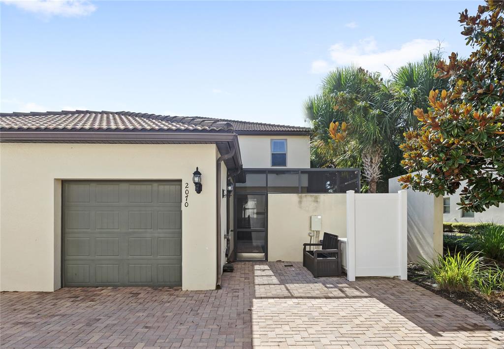 A beige house exterior features a gray garage door, a screened entryway, and brick pavers — 2070 ROME DRIVE, KISSIMMEE, FL