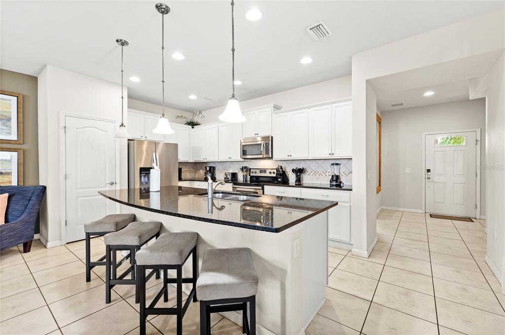 A kitchen features white cabinets, granite countertops, a center island with bar stools, and tile flooring — 2070 ROME DRIVE, KISSIMMEE, FL