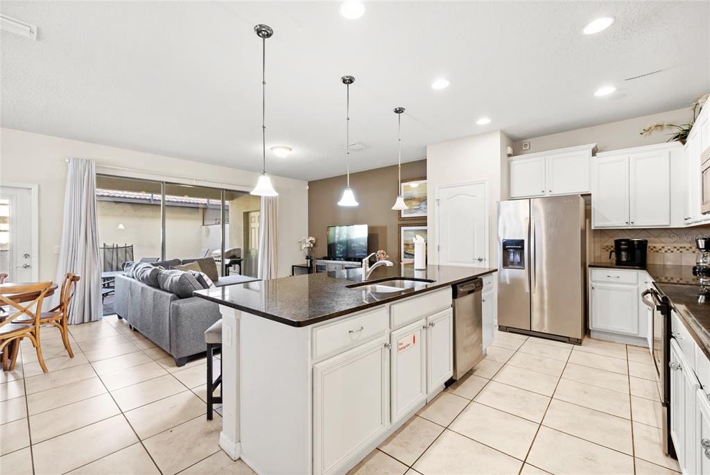 A kitchen with white cabinets, a granite-topped island, and stainless steel appliances overlooks a living area — 2070 ROME DRIVE, KISSIMMEE, FL