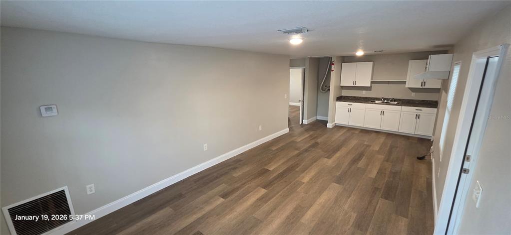 This room features wood-look flooring, light gray walls, and a small kitchen area with white cabinets — 603 W 27TH AVENUE, BRADENTON, FL