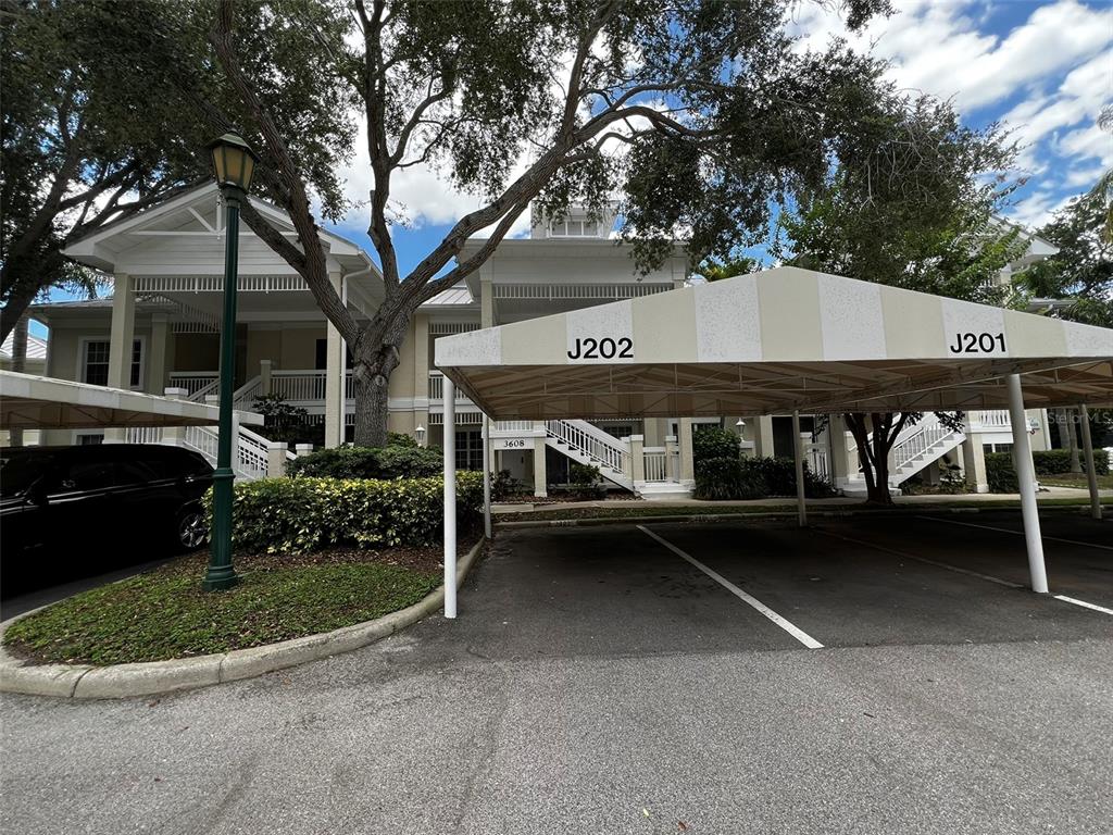 A covered parking area sits in front of a multi-story residential building with exterior staircases — 3608 54TH DRIVE W UNIT 202, BRADENTON, FL