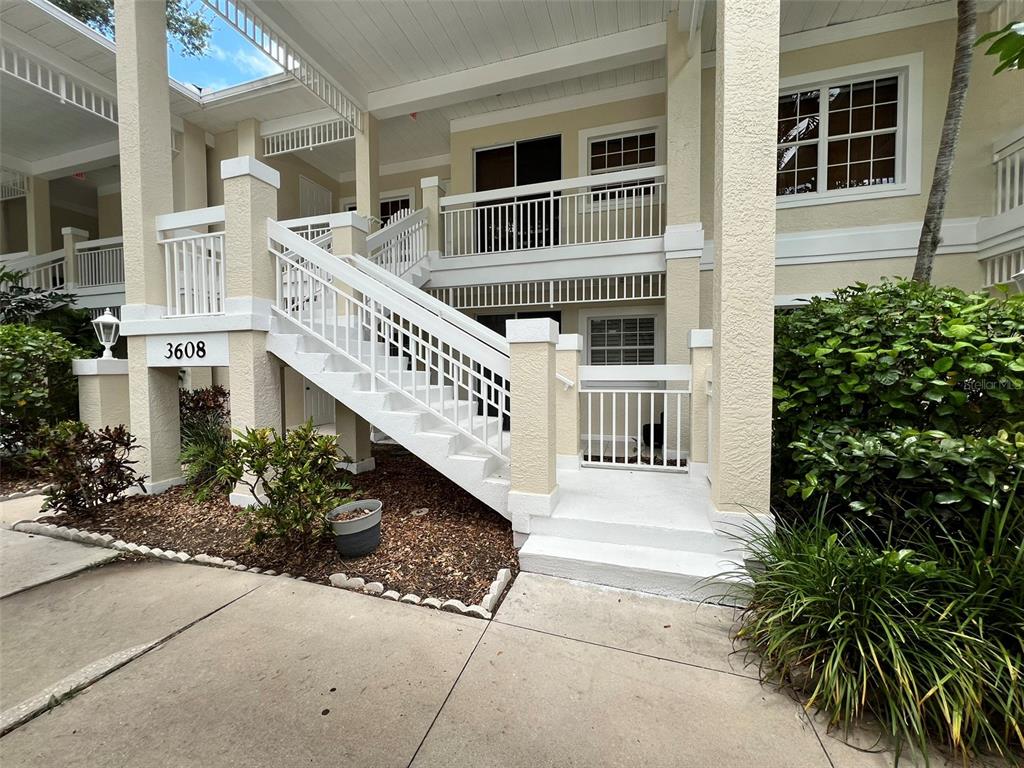 An exterior view of a two-story building with a white staircase leading to the upper level — 3608 54TH DRIVE W UNIT 202, BRADENTON, FL