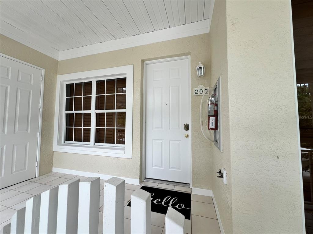 A white front door with a fire extinguisher mounted on the adjacent exterior wall — 3608 54TH DRIVE W UNIT 202, BRADENTON, FL