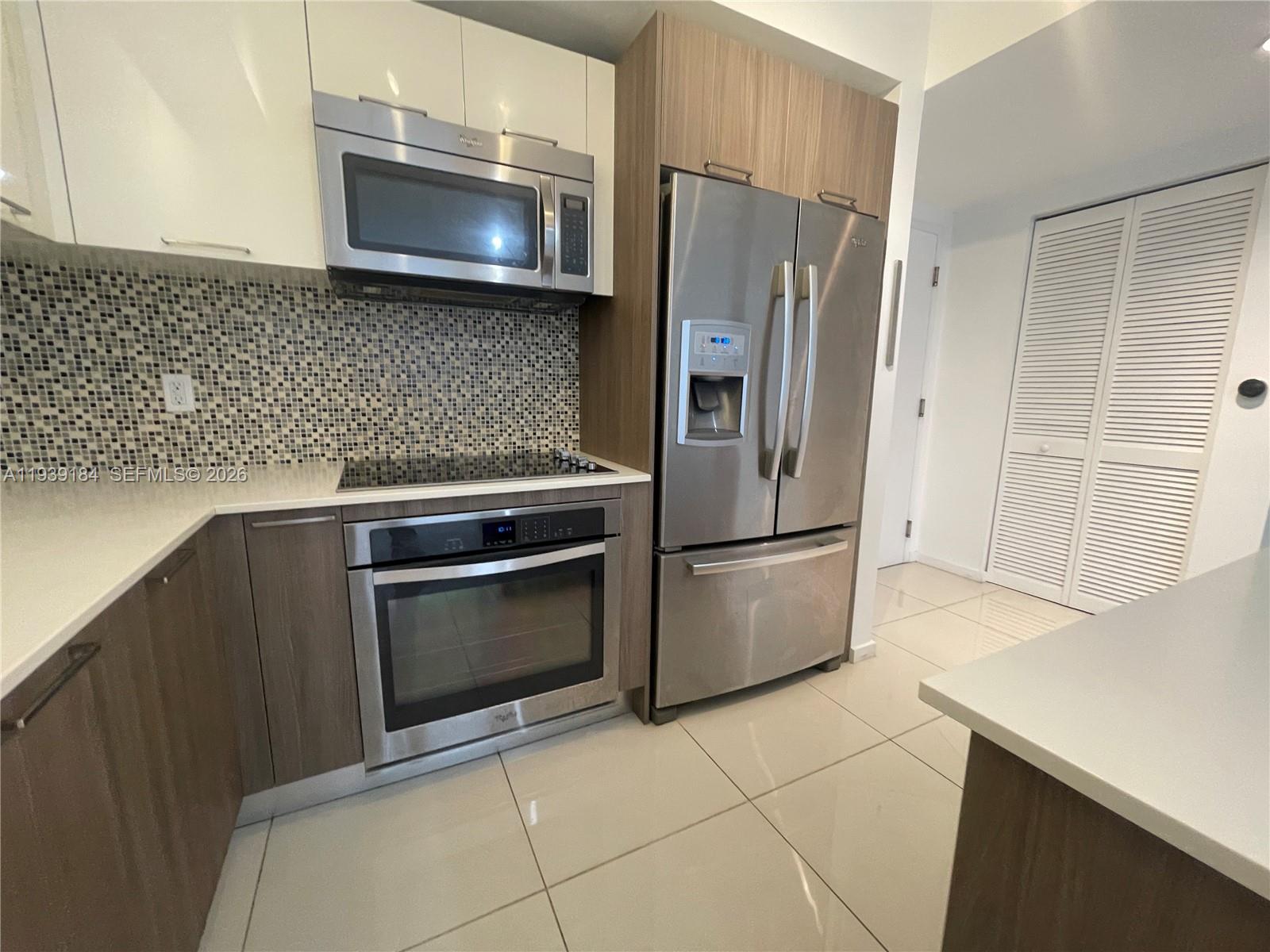 A modern kitchen features stainless steel appliances, wood-toned cabinetry, and a mosaic tile backsplash — 5252 NW 85th Ave # 1109, Doral FL 33166, DORAL, FL