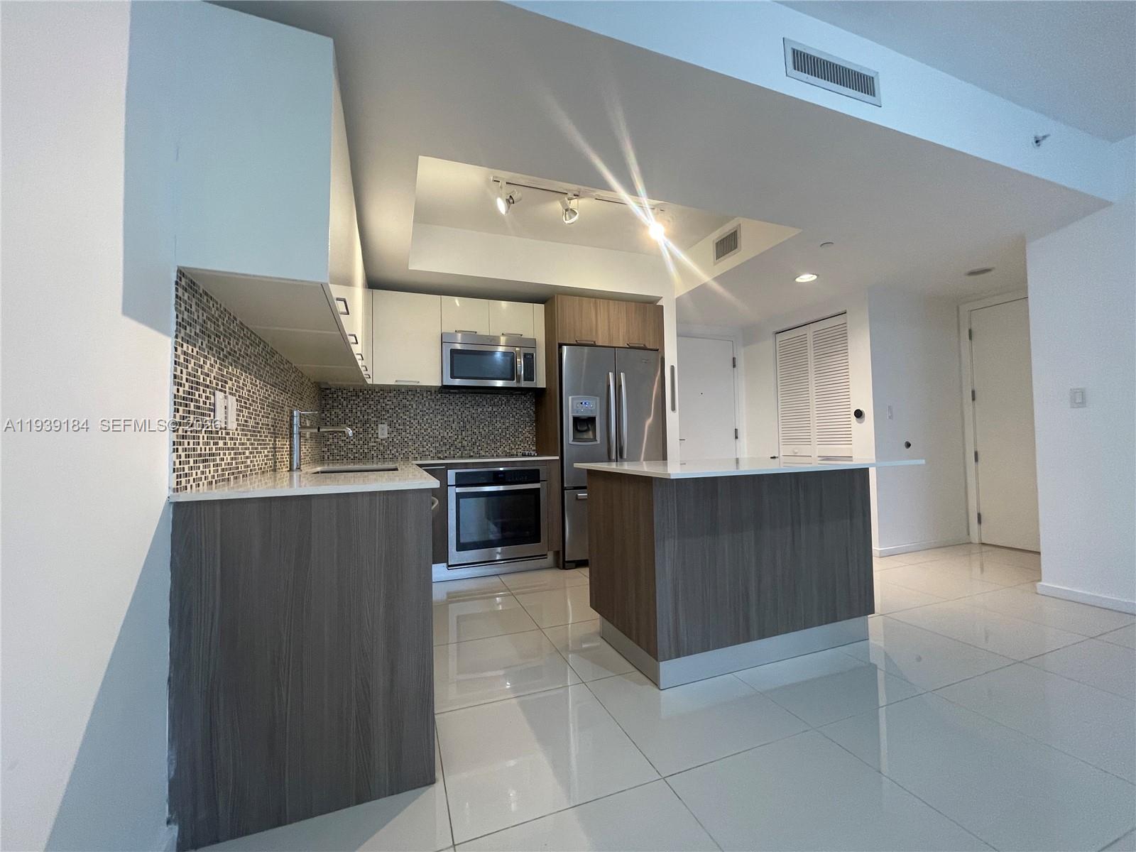 A modern kitchen features wood-tone cabinetry, white countertops, stainless steel appliances, and tiled flooring — 5252 NW 85th Ave # 1109, Doral FL 33166, DORAL, FL