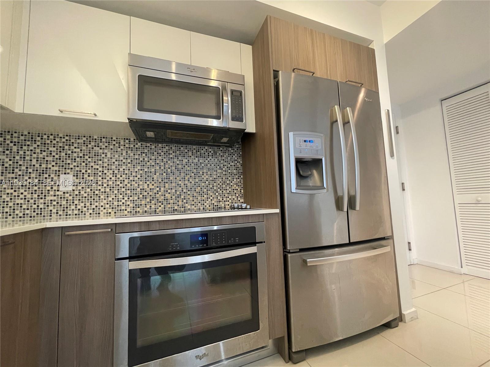 A kitchen features stainless steel appliances, wood-toned cabinets, white upper cabinets, and a mosaic backsplash — 5252 NW 85th Ave # 1109, Doral FL 33166, DORAL, FL
