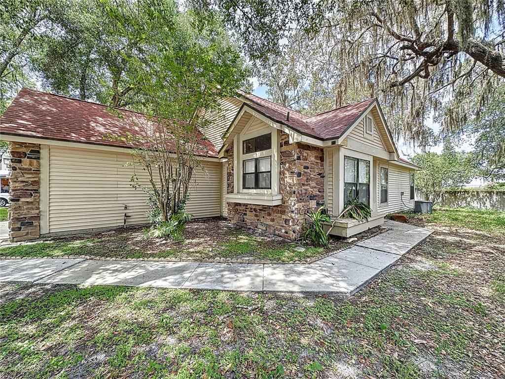 A single-story house exterior features tan siding, stone accents, and a red shingled roof — 5392 ROCKING HORSE PLACE, OVIEDO, FL