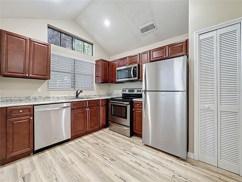 A kitchen features dark wood cabinets, stainless steel appliances, granite countertops, and light wood flooring — 5392 ROCKING HORSE PLACE, OVIEDO, FL
