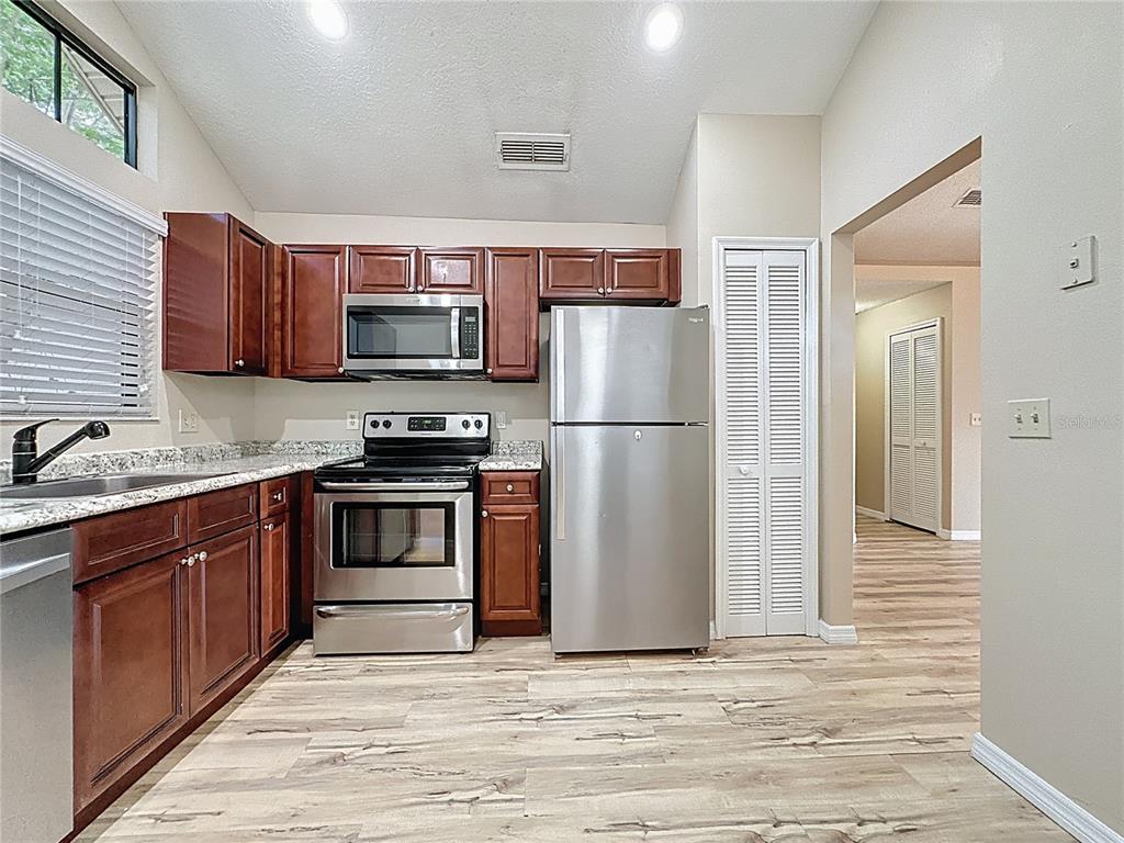 A kitchen features dark wood cabinets, stainless steel appliances, and light-colored wood-look flooring — 5392 ROCKING HORSE PLACE, OVIEDO, FL