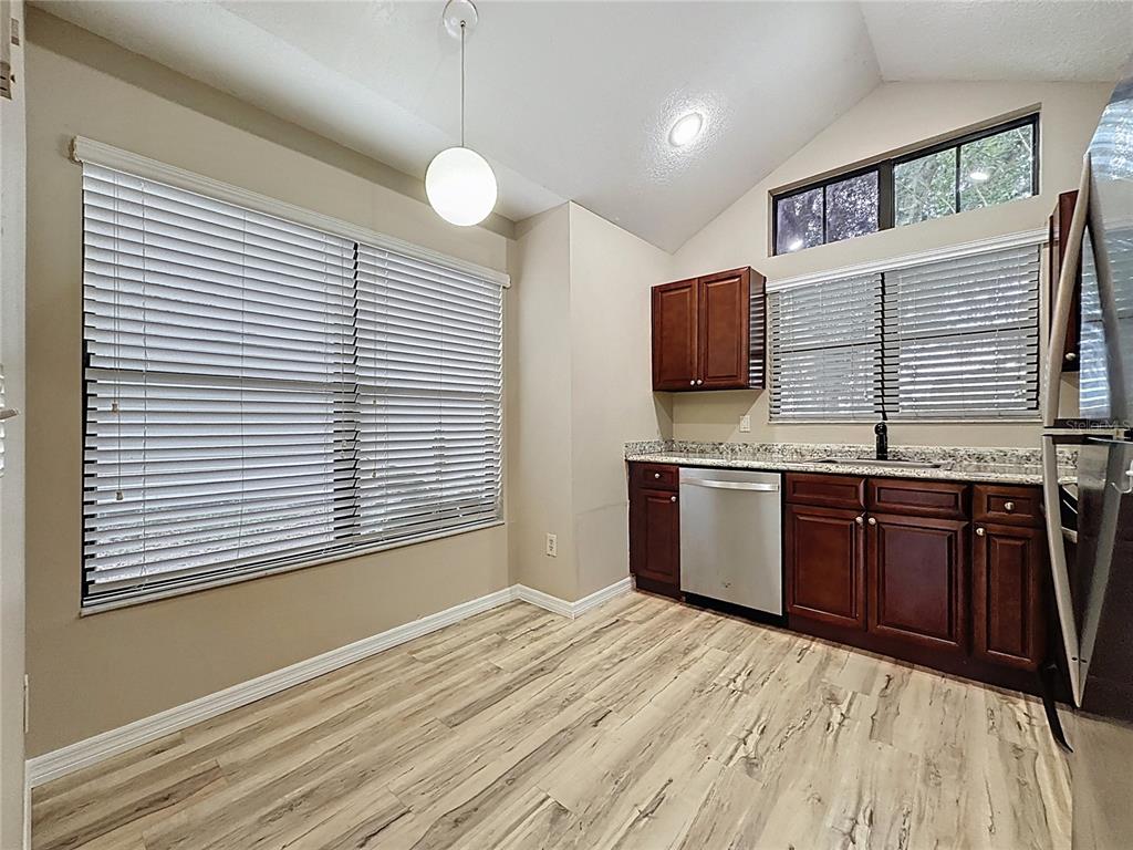A kitchen featuring dark wood cabinets, granite countertops, stainless steel appliances, and light wood flooring — 5392 ROCKING HORSE PLACE, OVIEDO, FL