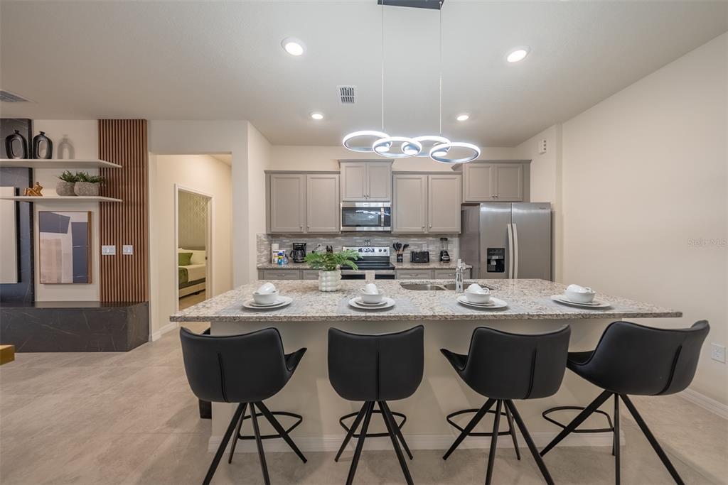 A modern kitchen features a granite-topped island with four black stools and gray cabinetry — 4470 KAIPO ROAD, DAVENPORT, FL