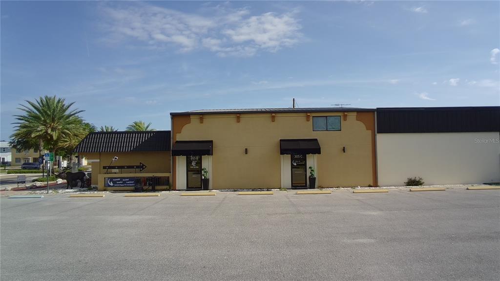 A tan commercial building with two black-awning entrances sits behind a large paved parking lot — 305 MAIN STREET UNIT A, B & C, AUBURNDALE, FL