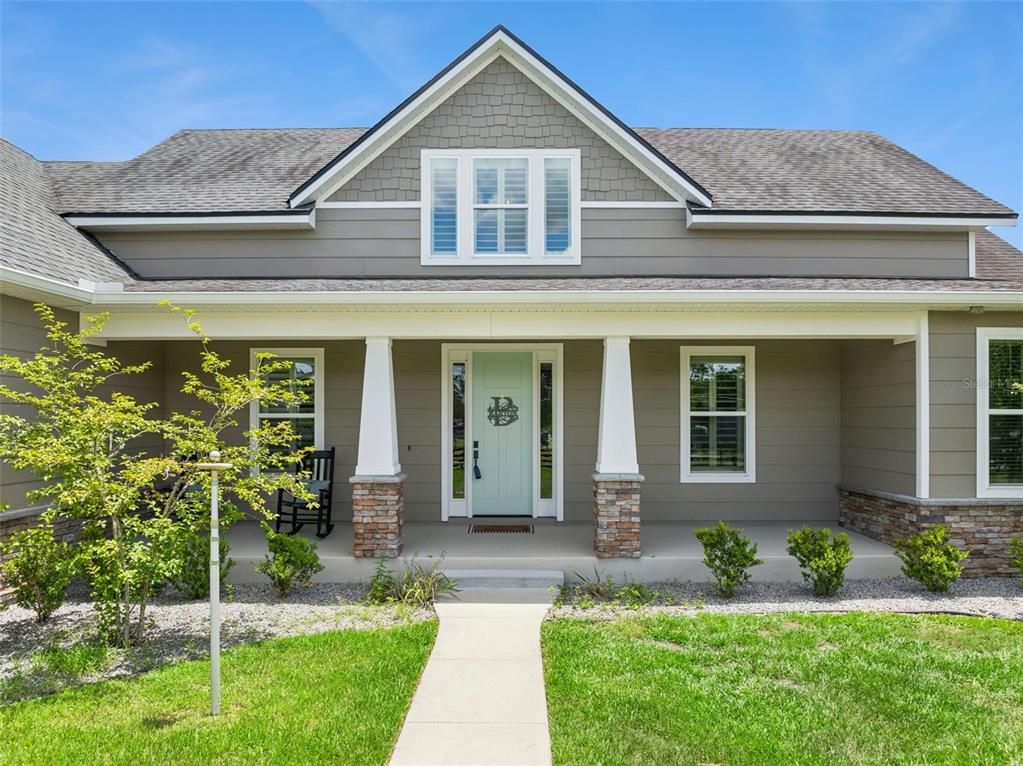 A front view of a gray house with a covered porch, stone pillars, and a light-colored door — 3454 IMPERIAL AVENUE, ST CLOUD, FL
