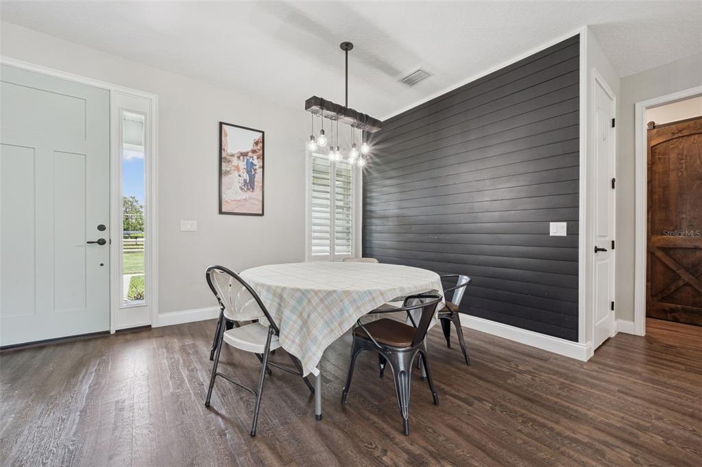 A dining area features a round table, a dark shiplap accent wall, and a chandelier — 3454 IMPERIAL AVENUE, ST CLOUD, FL