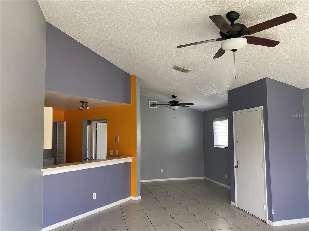 A living room with gray walls, tile flooring, two ceiling fans, and an orange accent wall — 2508 WOODGATE BOULEVARD UNIT 201, ORLANDO, FL