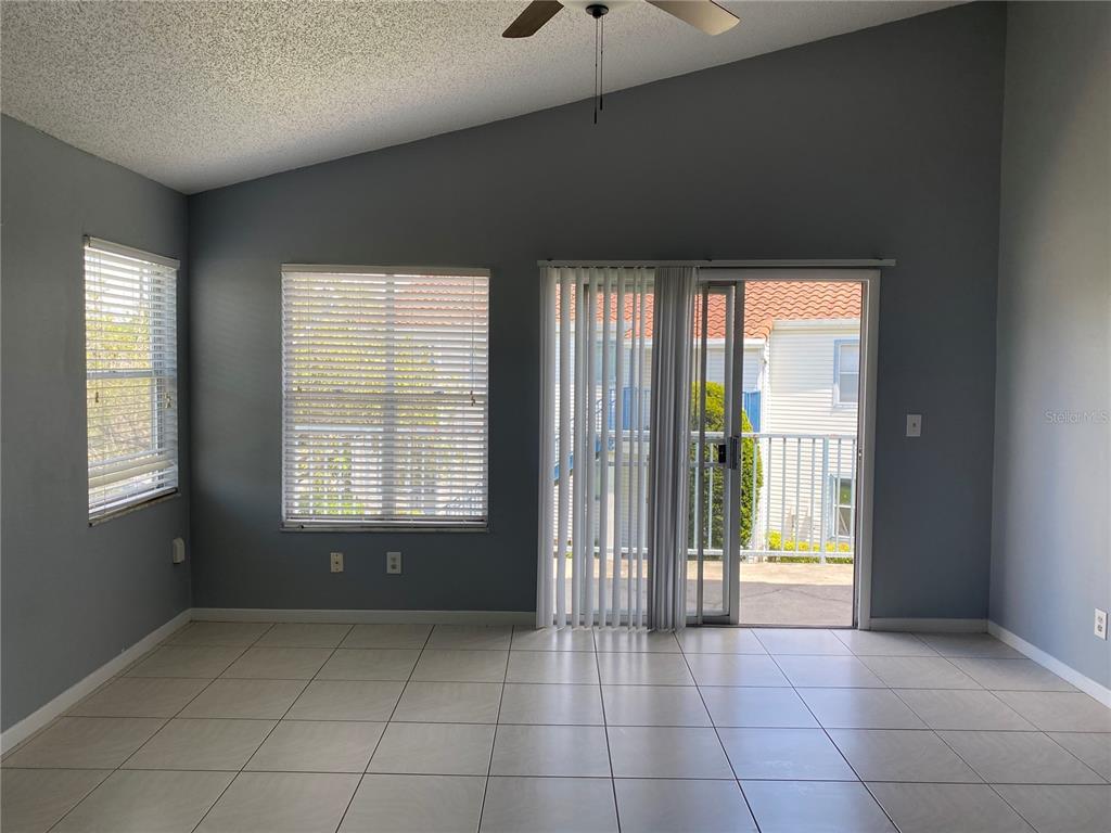 A living room with gray walls, tile flooring, a vaulted ceiling, and sliding glass doors — 2508 WOODGATE BOULEVARD UNIT 201, ORLANDO, FL