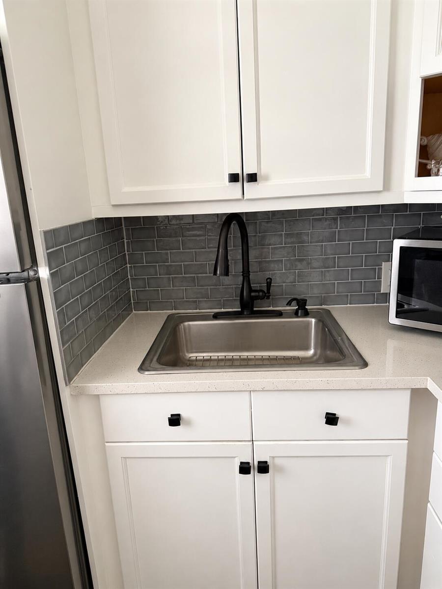 A kitchen sink area features white cabinets, a grey subway tile backsplash, and a black faucet — 256 Preston G, Boca Raton FL 33434, BOCA RATON, FL