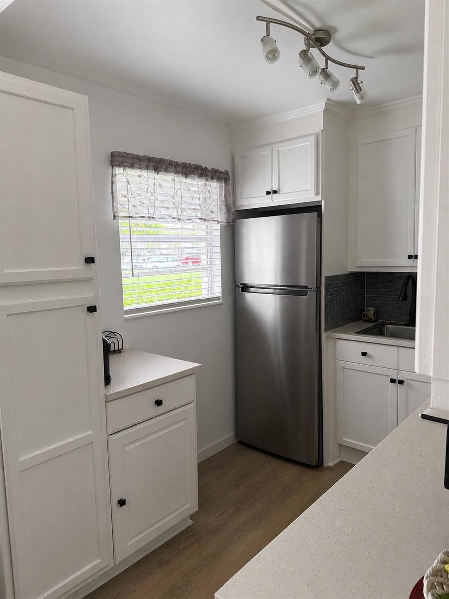 A kitchen features white cabinetry, stainless steel appliances, a gray subway tile backsplash, and wood-look flooring — 256 Preston G, Boca Raton FL 33434, BOCA RATON, FL