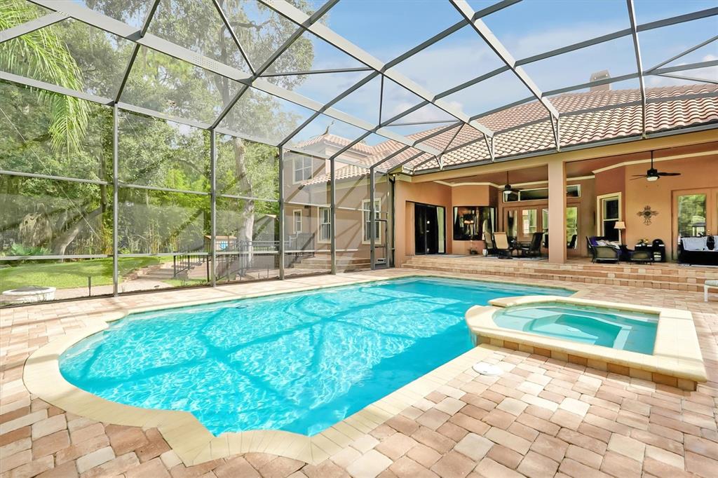 A swimming pool and spa are enclosed by a screened lanai behind a two-story house — 12012 RAMBLING OAK BOULEVARD, ORLANDO, FL