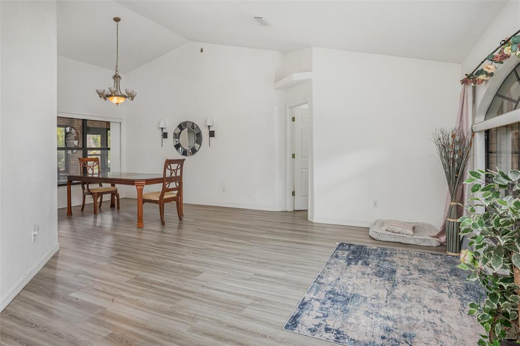 A dining area and living space feature vaulted ceilings, light wood flooring, and large windows — 1356 CANARY DRIVE, DELAND, FL