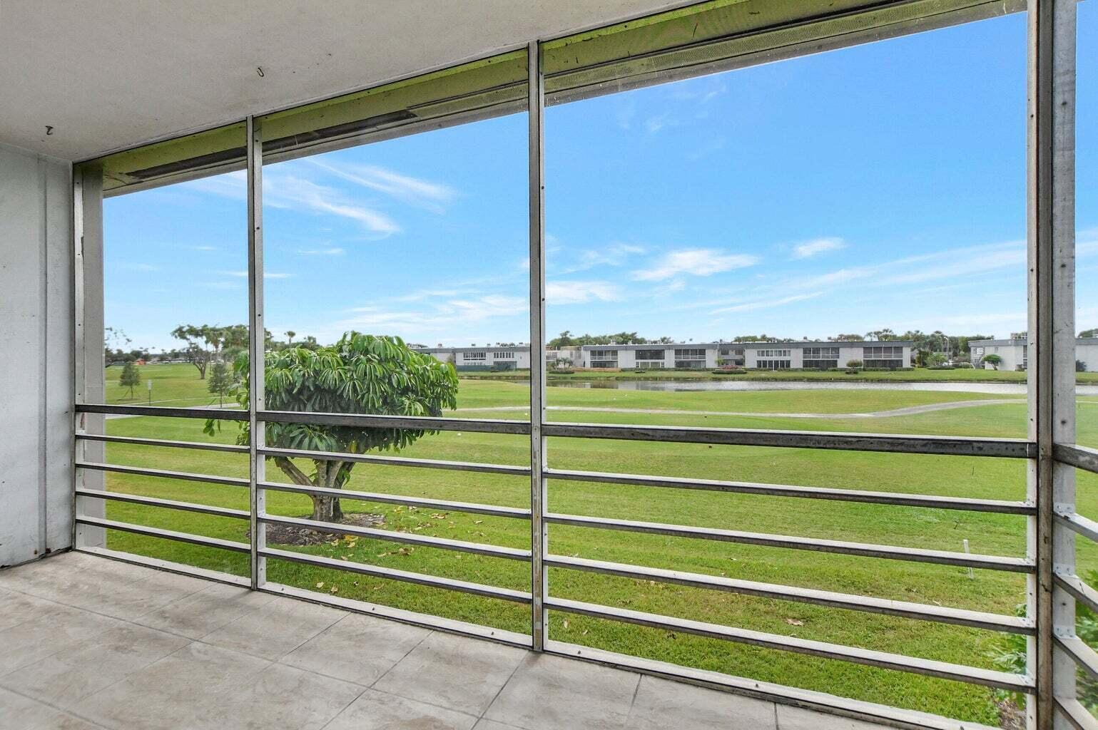 A screened-in balcony overlooks a grassy lawn, a small pond, and distant apartment buildings — 187 Normandy D, Delray Beach FL 33484, DELRAY BEACH, FL