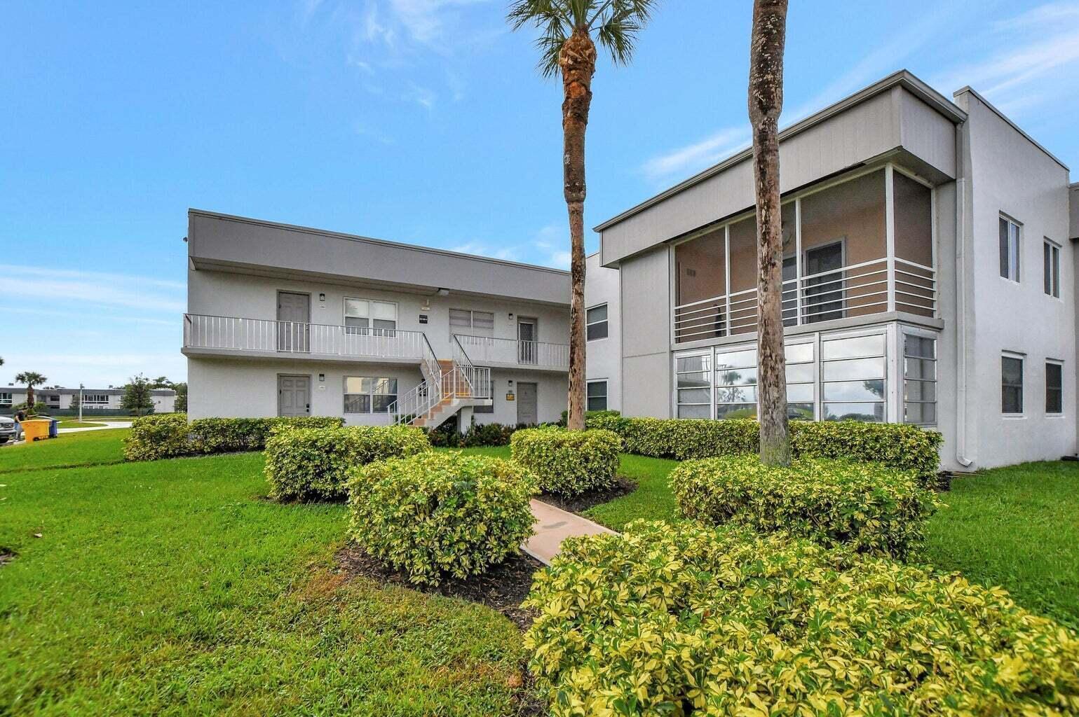 A two-story apartment building with a screened balcony, palm trees, and manicured landscaping — 187 Normandy D, Delray Beach FL 33484, DELRAY BEACH, FL