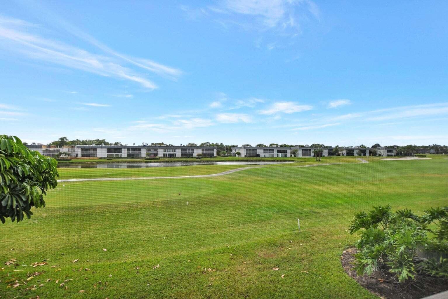 A view of a green golf course with a pond and residential buildings in the distance — 187 Normandy D, Delray Beach FL 33484, DELRAY BEACH, FL