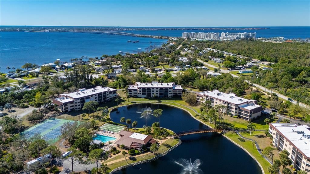 An aerial view shows apartment buildings surrounding a pond with fountains and a tennis court — 23465 HARBORVIEW ROAD UNIT 724, PUNTA GORDA, FL