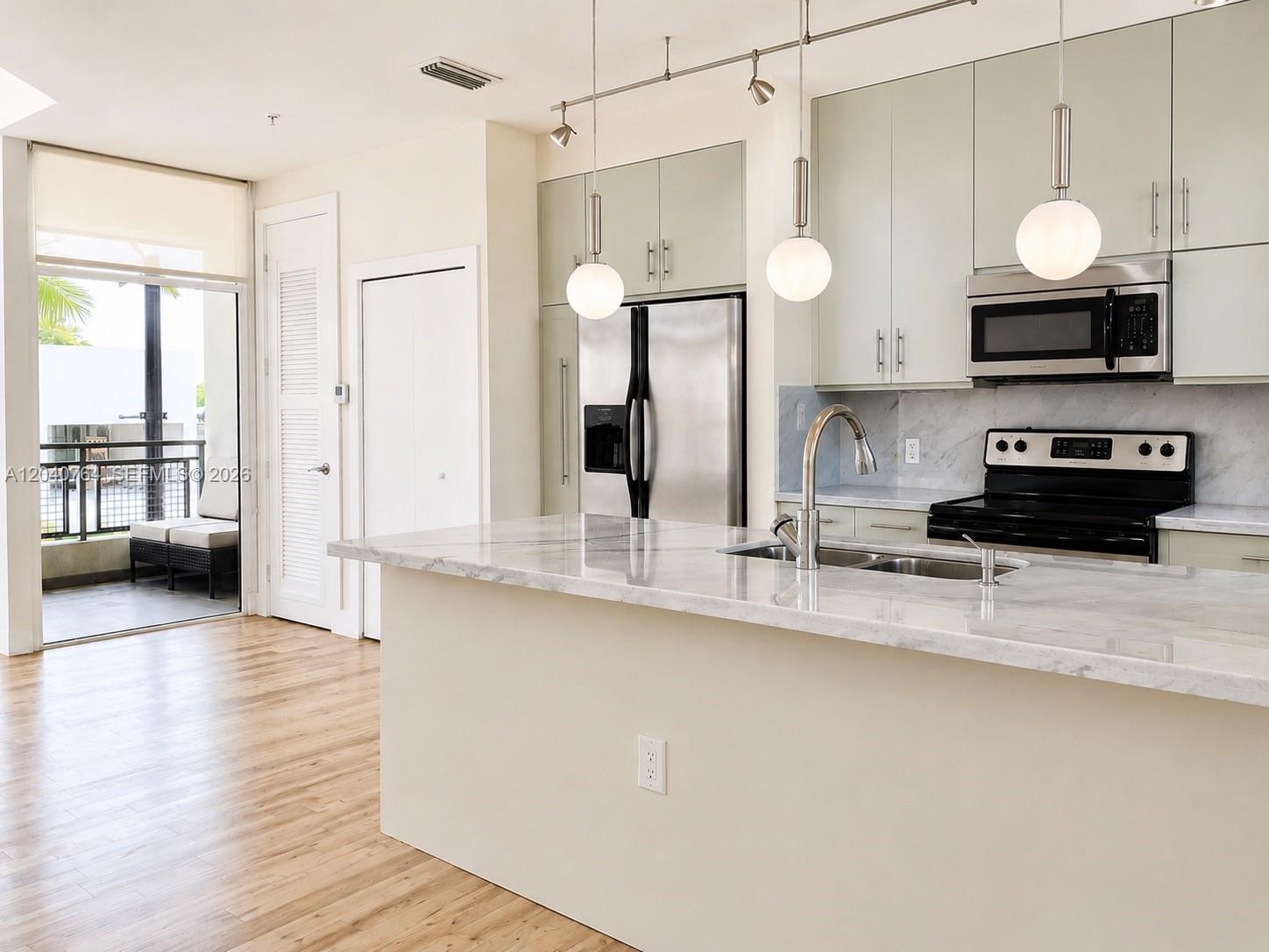 A modern kitchen features a marble-topped island, stainless steel appliances, and an adjacent balcony — 6701 Biscayne Blvd # 201, Miami FL 33138, MIAMI, FL