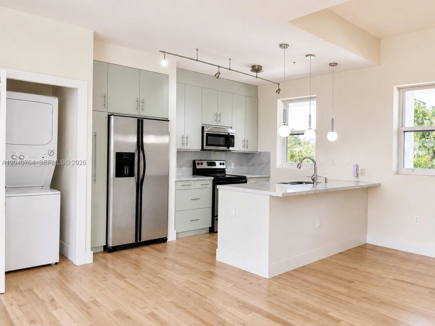 A modern kitchen features light green cabinetry, stainless steel appliances, and a marble-topped island — 6701 Biscayne Blvd # 201, Miami FL 33138, MIAMI, FL
