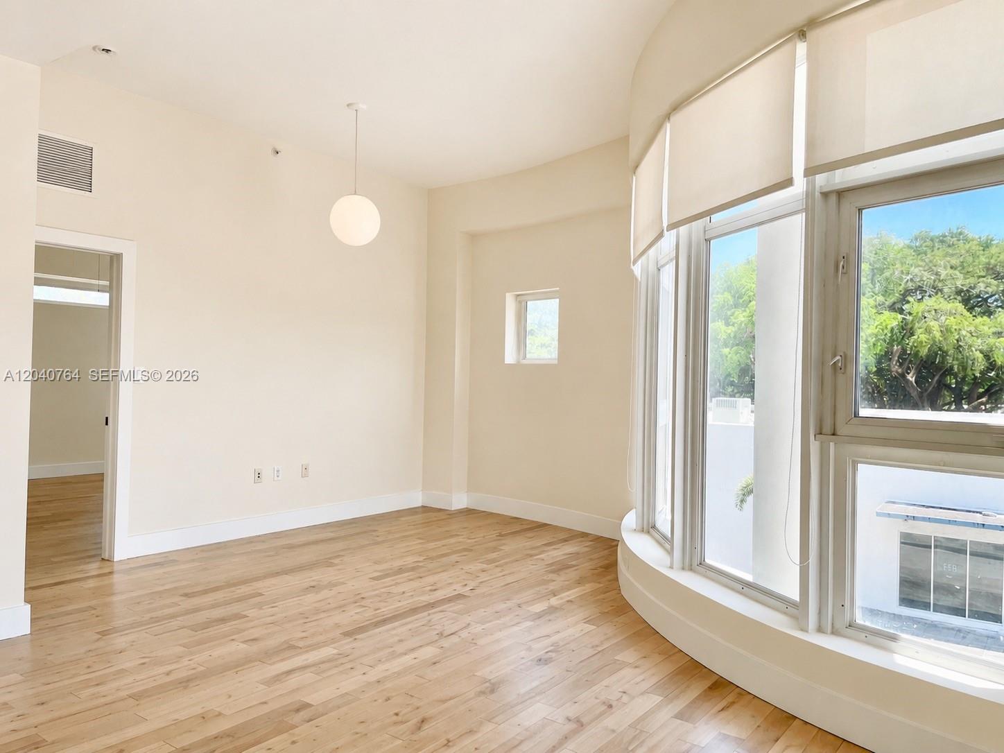 An empty room features light wood flooring, a curved window wall, and a pendant light — 6701 Biscayne Blvd # 201, Miami FL 33138, MIAMI, FL