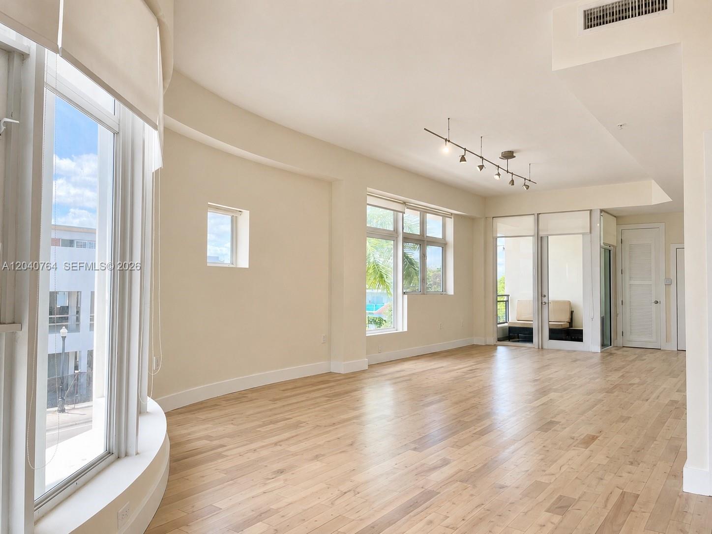 An empty living room features light hardwood floors, large windows, and a track lighting fixture — 6701 Biscayne Blvd # 201, Miami FL 33138, MIAMI, FL