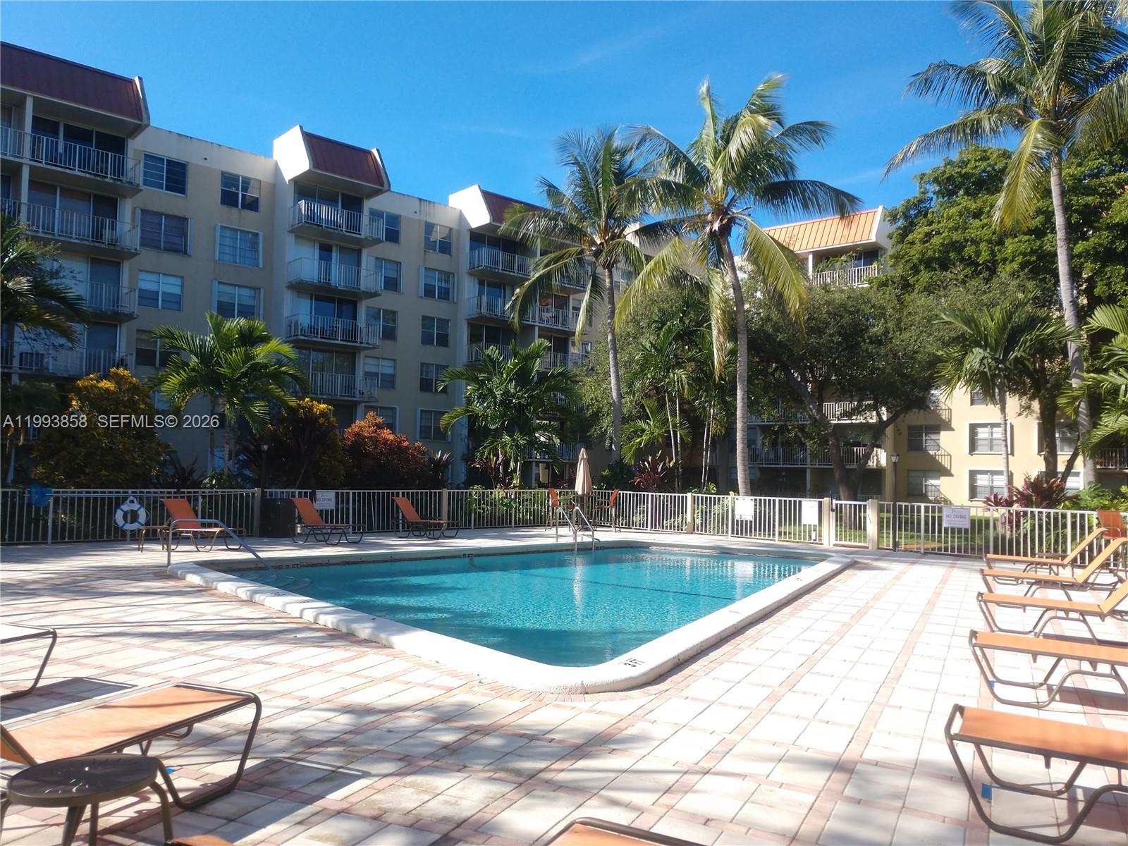 A swimming pool is surrounded by lounge chairs and palm trees in front of apartment buildings — 13100 SW 92nd Ave # 112, Miami FL 33176, MIAMI, FL