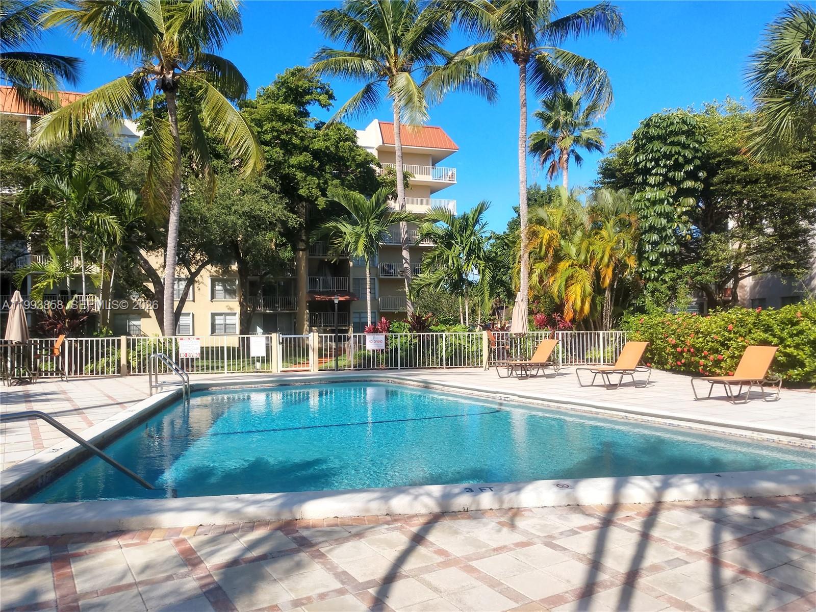 A swimming pool with lounge chairs sits in front of a multi-story apartment building — 13100 SW 92nd Ave # 112, Miami FL 33176, MIAMI, FL