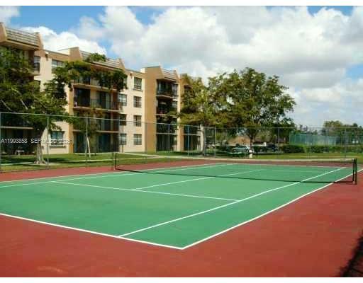 A tennis court with a green surface and red borders sits before a multi-story apartment building — 13100 SW 92nd Ave # 112, Miami FL 33176, MIAMI, FL