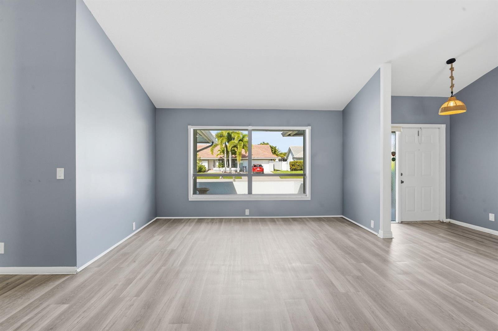 An empty room with light blue walls, gray wood-look flooring, and a large front window — 9284 Laurel Green Drive, Boynton Beach FL 33437, BOYNTON BEACH, FL