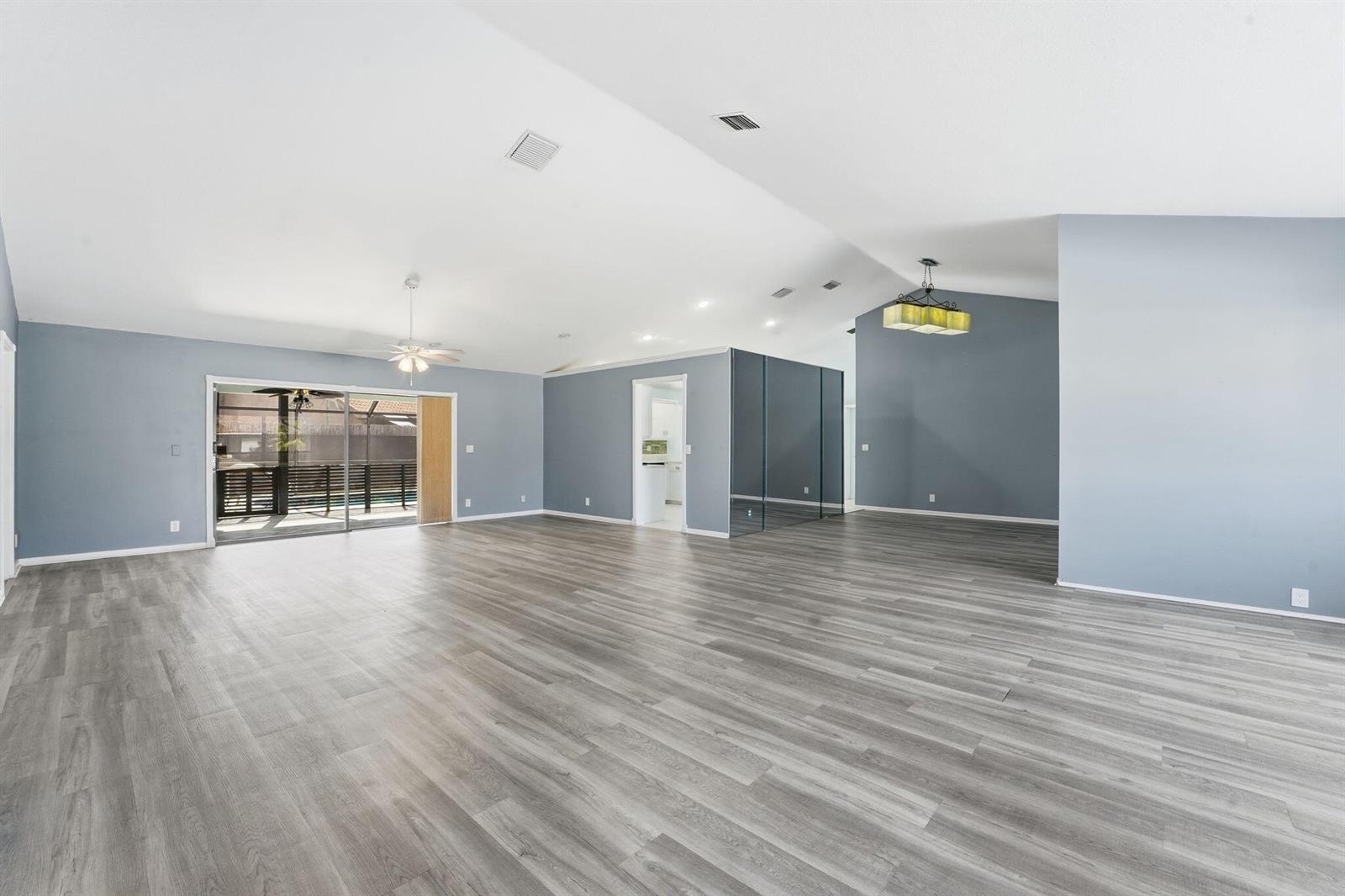 A spacious living area features gray walls, wood-look flooring, a vaulted ceiling, and sliding doors — 9284 Laurel Green Drive, Boynton Beach FL 33437, BOYNTON BEACH, FL