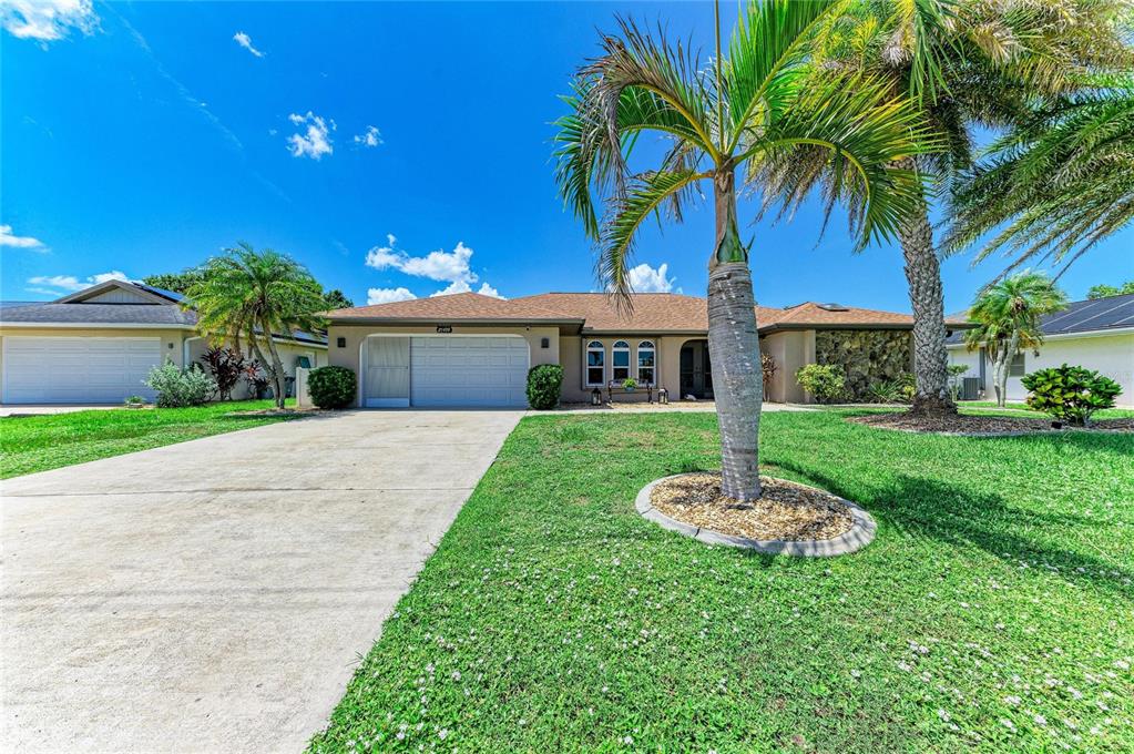 A beige house exterior features arched windows, a metal bench, and a gravel front yard — 25499 TERRAIN LANE, PUNTA GORDA, FL