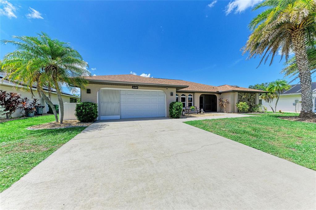 A paved patio sits in a grassy backyard next to a screened-in pool enclosure — 25499 TERRAIN LANE, PUNTA GORDA, FL