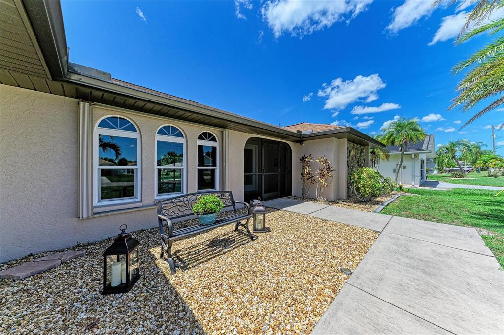 A grassy backyard features a paver patio, palm trees, and a screened-in pool enclosure — 25499 TERRAIN LANE, PUNTA GORDA, FL