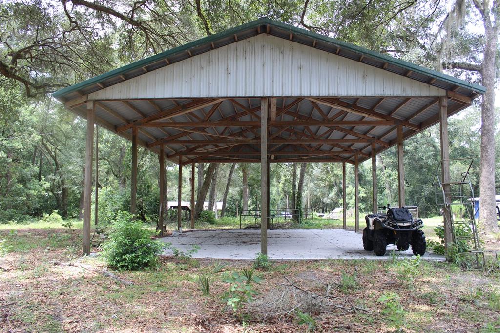 An open-sided metal pole barn with a concrete slab floor sits in a wooded area — 29160 SE 150TH STREET, ALTOONA, FL