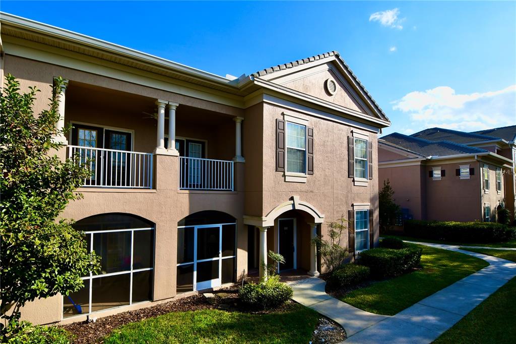 A two-story tan stucco building with a screened-in patio, upper balcony, and arched entryway — 14214 FREDRICKSBURG DRIVE UNIT 108, ORLANDO, FL