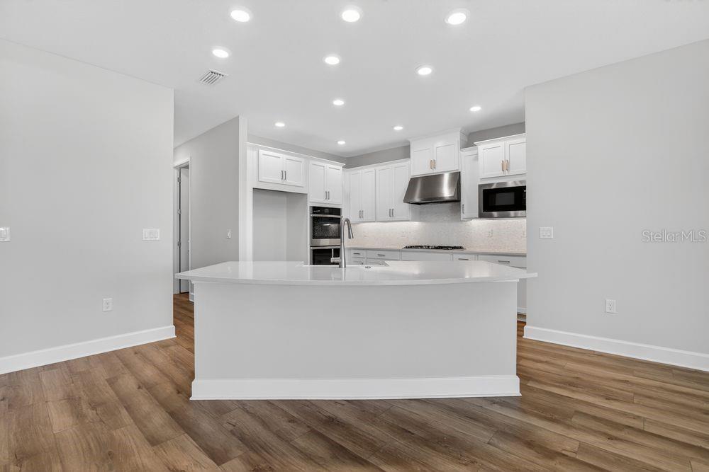 A modern kitchen features white cabinets, stainless steel appliances, and a central island with countertops — 656 JUNONIA BOULEVARD, NEW SMYRNA BEACH, FL