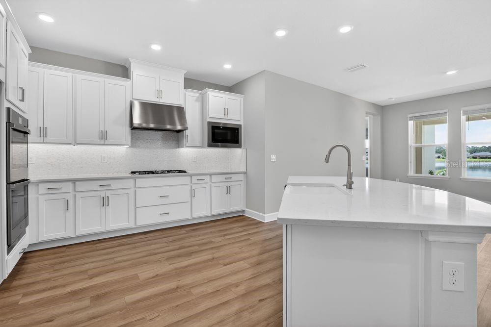 A modern kitchen features white cabinetry, quartz countertops, stainless steel appliances, and wood-look flooring — 656 JUNONIA BOULEVARD, NEW SMYRNA BEACH, FL