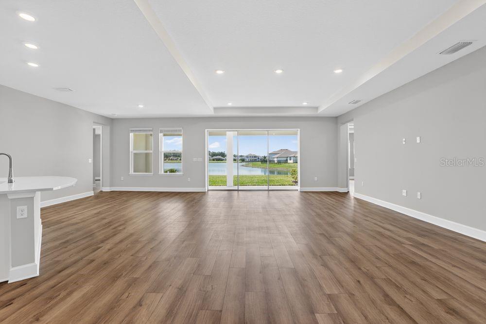An open-concept living area features light gray walls, wood-look flooring, and sliding glass doors — 656 JUNONIA BOULEVARD, NEW SMYRNA BEACH, FL