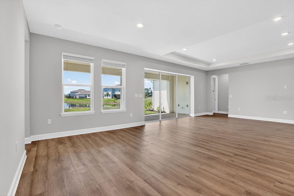 An empty living room with light gray walls, wood-look flooring, and sliding glass patio doors — 656 JUNONIA BOULEVARD, NEW SMYRNA BEACH, FL