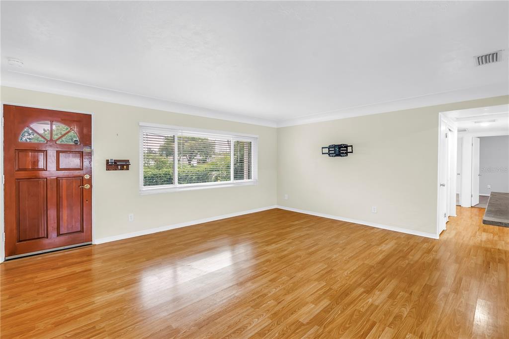 An empty living room features hardwood floors, a large window, and a wooden front door — 6195 28TH AVENUE N, ST PETERSBURG, FL