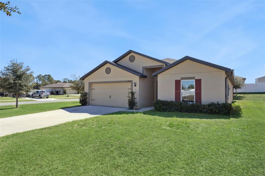 A single-story house with a tan stucco exterior, a two-car garage, and a front lawn — 12023 INDIAN GRASS WAY, LEESBURG, FL