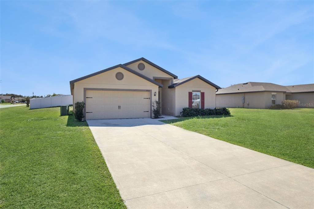 A single-story house with a beige stucco exterior, a two-car garage, and a concrete driveway — 12023 INDIAN GRASS WAY, LEESBURG, FL