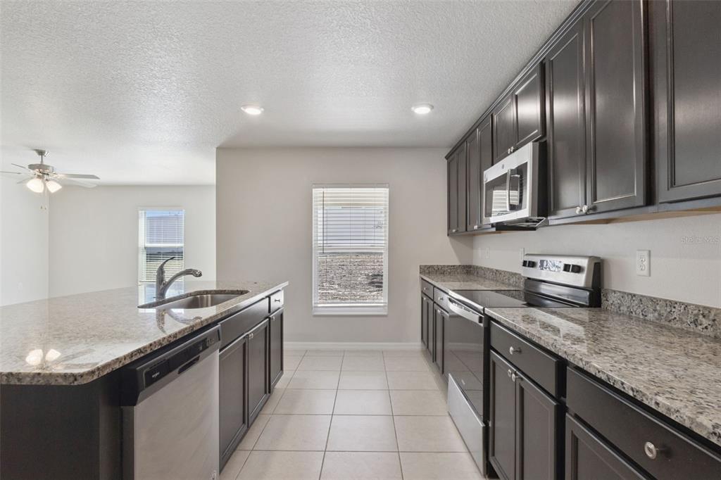 A kitchen with dark cabinets, granite countertops, stainless steel appliances, and light tile flooring — 12023 INDIAN GRASS WAY, LEESBURG, FL
